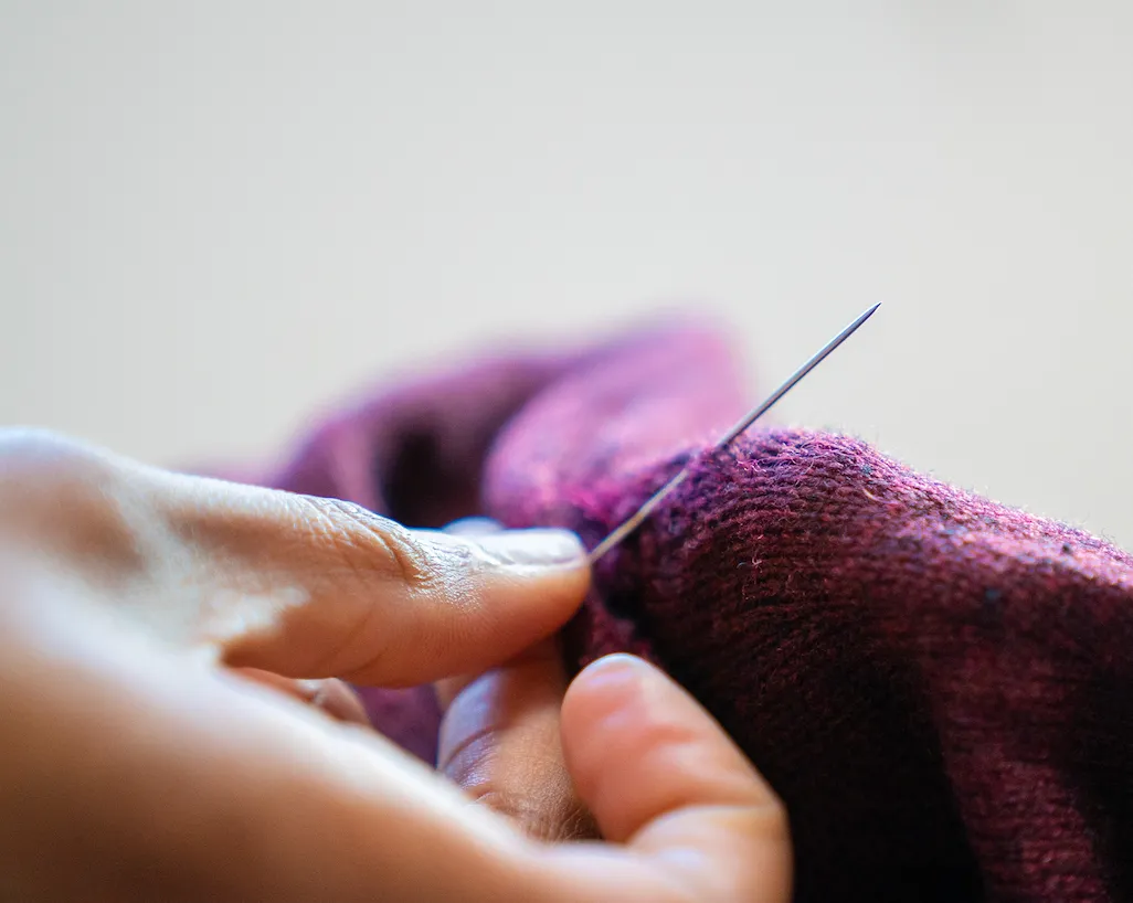 SOJO Tailor repairing a shirt with needle and thread
